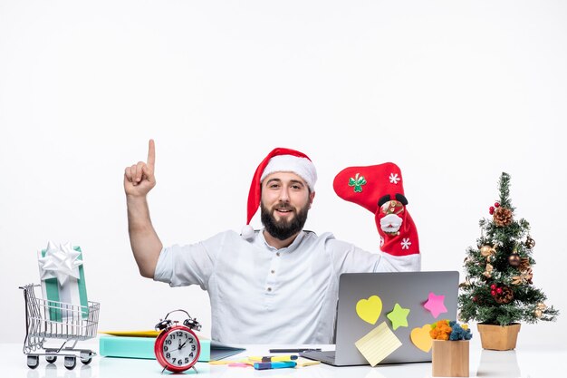 산타클로스 모자를 쓰고 크리스마스 양말을 손에 들고 사무실에서 위를 가리키는 긍정적인 젊은 성인과 함께하는 크리스마스 분위기