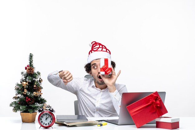 Xmas mood with surprised business person with santa claus hat raising his gift to his face and checking his tme on white background