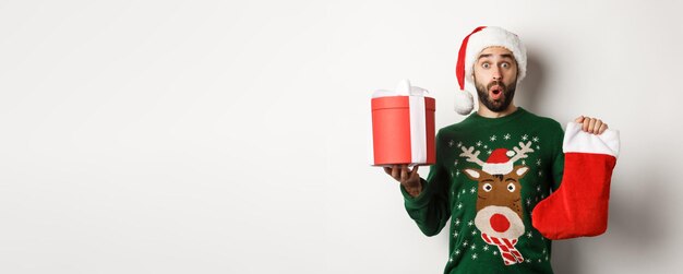 Free photo xmas and winter holidays concept excited man holding christmas sock and gift box celebrating new yea