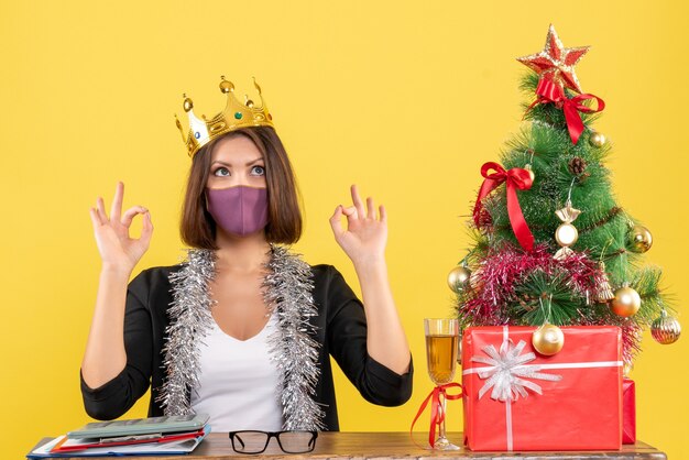 Xsmas mood with beautiful lady in suit with medical mask and wearing mask making eyeglasses gesture in the office on yellow 