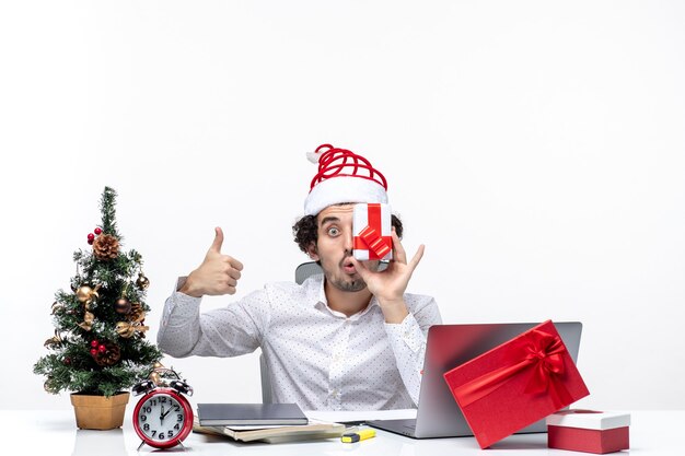 산타 클로스 모자가 그의 얼굴에 그의 선물을 제기하고 흰색 배경에 완벽한 제스처를 만드는 재미있는 비즈니스 사람과 크리스마스 분위기