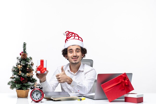 Xsmas mood with happy emotional young businessman with santa claus hat and raising his gift making ok gesture on white background