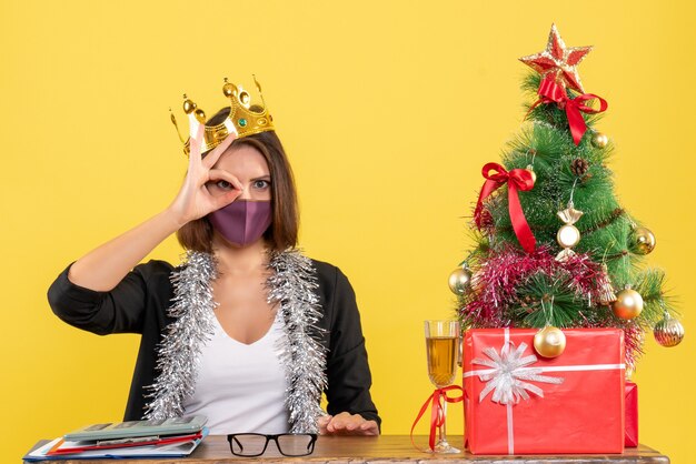 Xsmas mood with serious beautiful lady in suit with medical mask and wearing mask making spectacular gesture in the office on yellow 