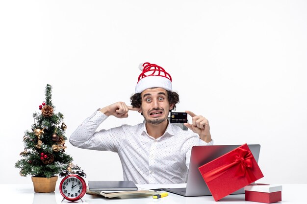 Xsmas mood with young bearded nervous business person with santa claus hat holding bank card and closing his ear in the office