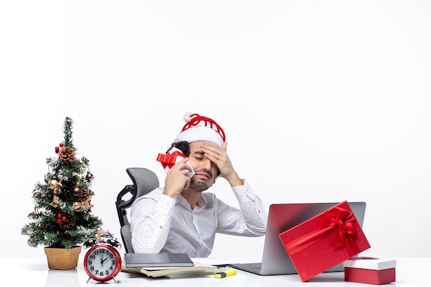 Umore di natale con giovane barbuto uomo d'affari nervoso scioccato con cappello di babbo natale alzando il suo regalo su sfondo bianco