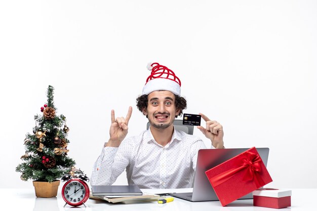 Рождественское настроение с молодым бородатым улыбающимся деловым человеком в шляпе санта-клауса, держащим банковскую карту и показывающим двоих на белом фоне