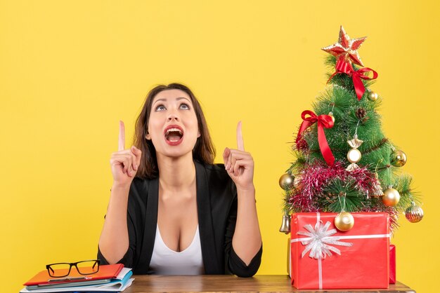 Xsmas mood with young concentrated beautiful woman pointing up and sitting at office