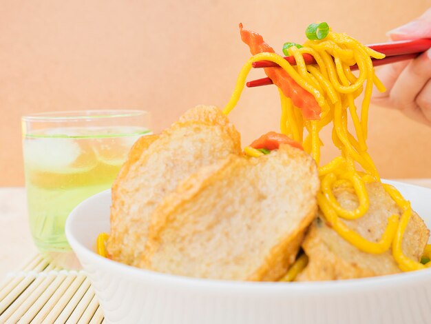 Yakisoba with glass of cold green tea over bamboo pad with chopstick and hand