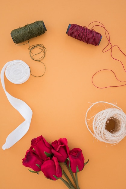 Yarn spools; white ribbon; string spool and red roses on an orange backdrop