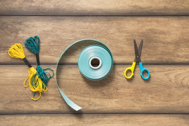 Yarn thread; ribbon and scissor on wooden backdrop