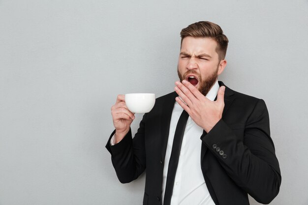 Yawning bearded man in suit drinking coffee