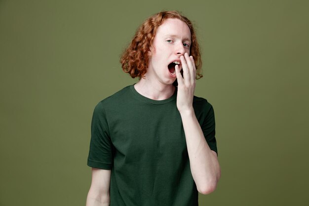 緑の背景に分離された緑のTシャツを着てあくびをする若いハンサムな男