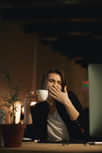 Yawning young woman designer sitting indoors