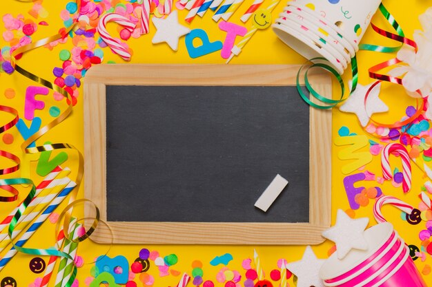 Yellow background with glasses, a chalkboard and party decoration