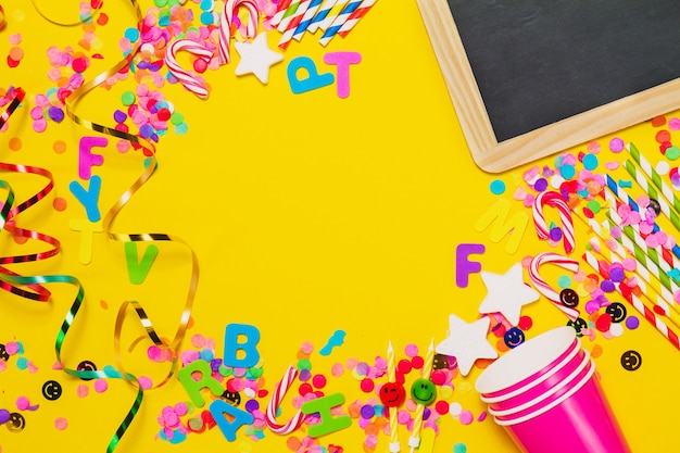 Yellow background with glasses, a chalkboard and party decoration