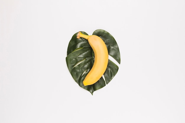 Желтый банан на зеленом листе в центре белой поверхности