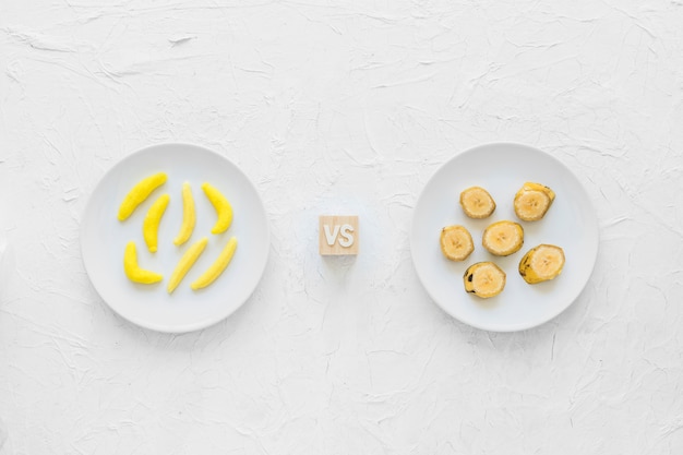 Yellow banana shaped gum candy versus banana slices on plate over textured background