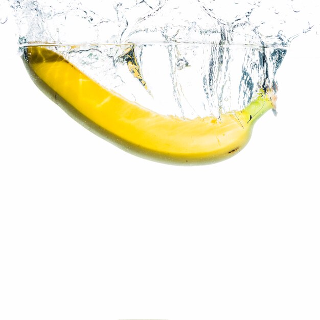 Yellow banana splashing into water against white background