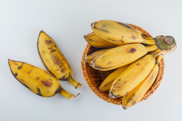 Yellow bananas in a wicker basket on a white.