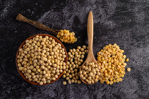 Yellow beans in a wooden bowl and wooden spoon on the black cement floor.