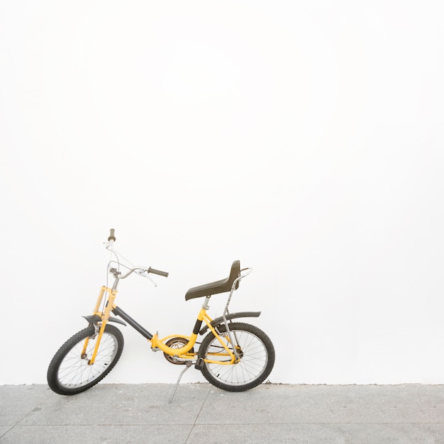 Yellow bicycle parked in front of white wall