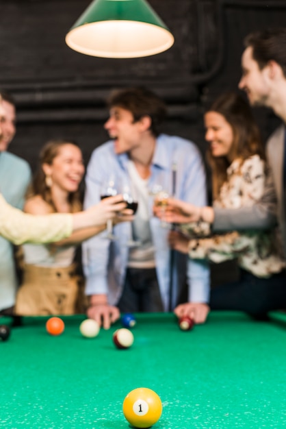 Yellow billiard ball with one number on snooker table in front of friends toasting wine