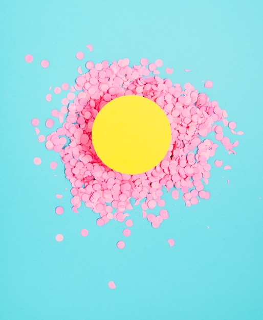 Желтый пустой круг кадр над праздничным маленьким розовым конфетти на синем фоне