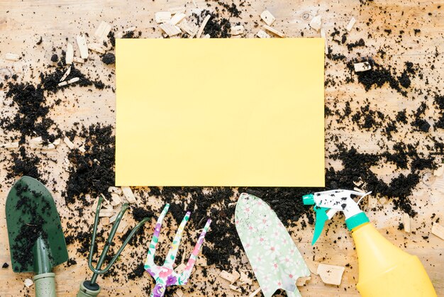 Yellow blank empty paper over soil with gardening equipments