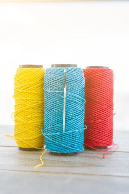 Yellow; blue and red yarn spool on wooden desk