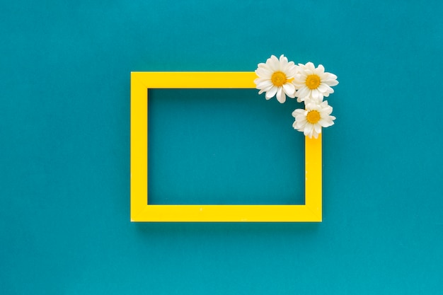 Foto gratuita blocco per grafici in bianco del bordo giallo decorato con i fiori della margherita bianca su priorità bassa blu