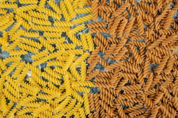 Yellow and brown raw fusilli pasta on blue space. 