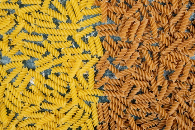 Yellow and brown raw fusilli pasta on blue space. 