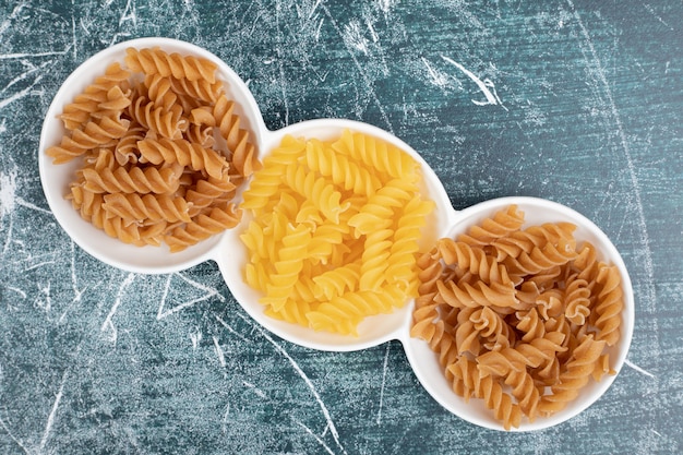 Yellow and brown raw fusilli pasta in white bowls. High quality photo