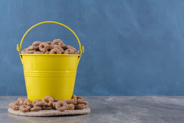 Un secchio giallo pieno di cereali gustosi sani su tela di sacco.