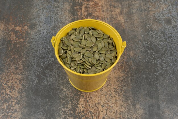 Yellow bucket full of pumpkin peeled seeds on marble surface