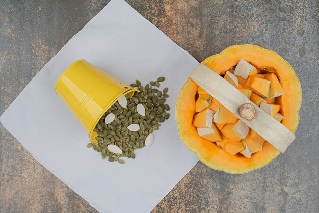 Yellow bucket full of pumpkin peeled seeds with fresh sliced pumpkin on marble wall