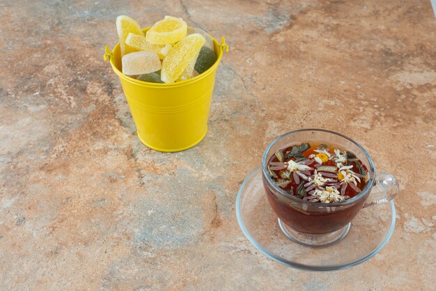 A yellow bucket full of sugar jelly candy and cup of herbal tea