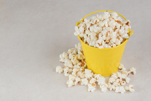 Foto gratuita secchio giallo troppo pieno di popcorn croccante sul tavolo di marmo.