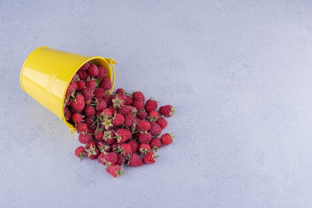 Yellow bucket of raspberries spilled over on marble background. High quality photo