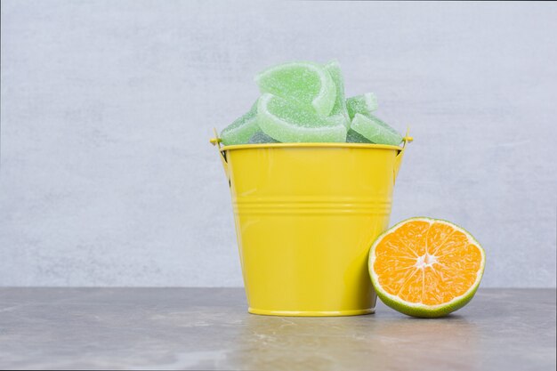 Yellow bucket with sugar marmalade and slice of orange on marble background.