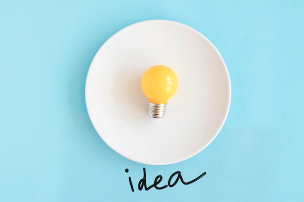 Yellow bulb on white plate with idea text on blue background