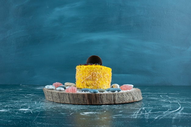 Free photo yellow cake and candy rocks on a board on blue.