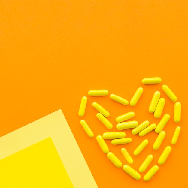 Yellow candy capsules forming heart shape on orange background