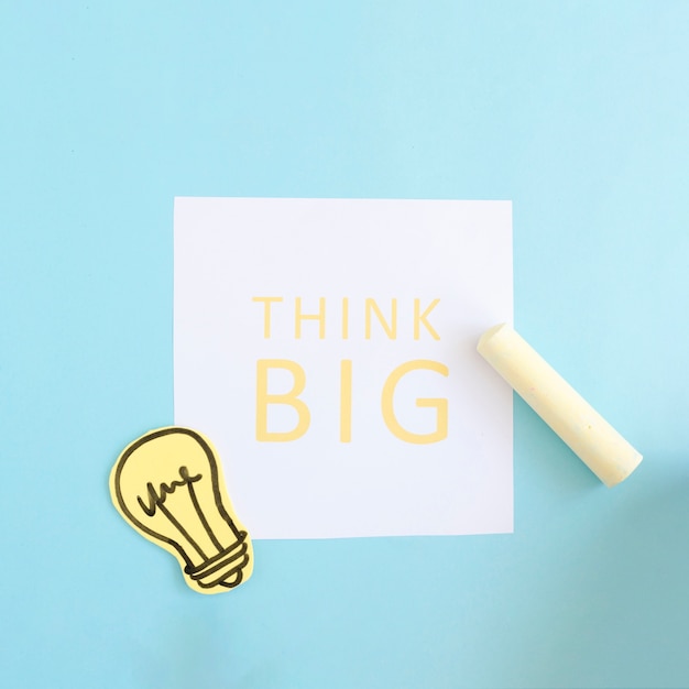 Free photo yellow chalk and paper cutout light bulb on think big text over white paper on blue background