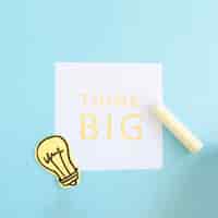 Free photo yellow chalk and paper cutout light bulb on think big text over white paper on blue background