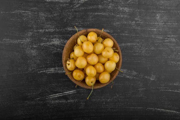 Yellow cherries in a wooden bowl on the board