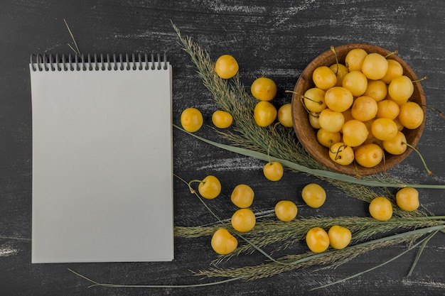 Free photo yellow cherries in a wooden bowl with a notebook aside