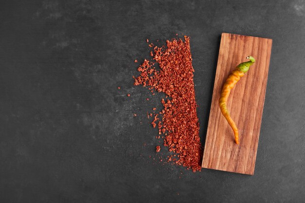 A yellow chili on a wooden platter with paprika aside. 