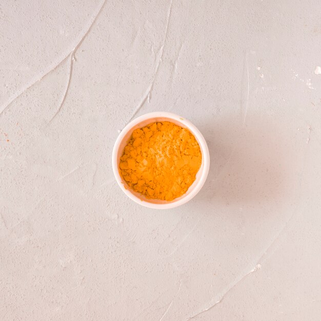 Yellow color powder in white bowl on concrete backdrop