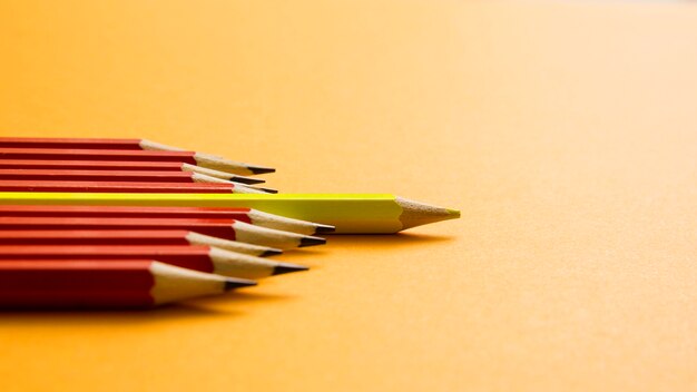 Yellow colored pencil lying between red pencil against yellow background